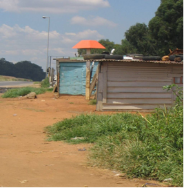 A pipeline, as indicated by the red marker pole, runs beneath makeshift housing (SASOL Gas, PIMSIS project).